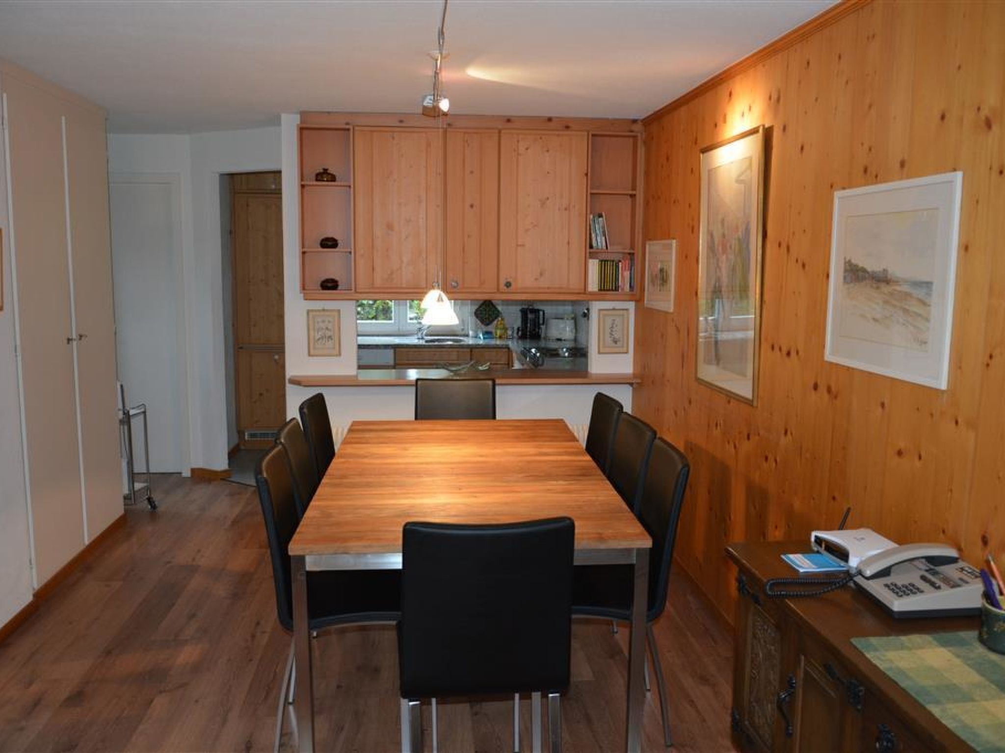 Ein Essbereich mit Holztisch und Stühlen, eine Küche mit Holzschränken und ein gerahmtes Bild an der Wand.