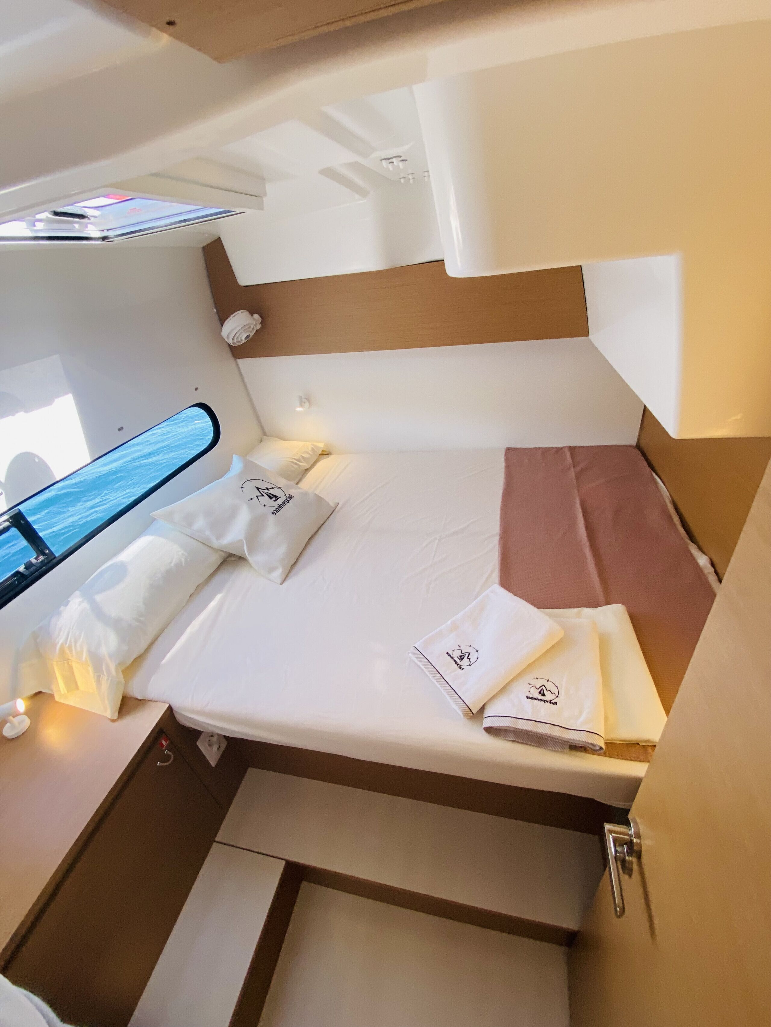 Ein kleiner, gut beleuchteter Raum mit einem Bett, Kissen und ordentlich gefalteten Handtüchern.