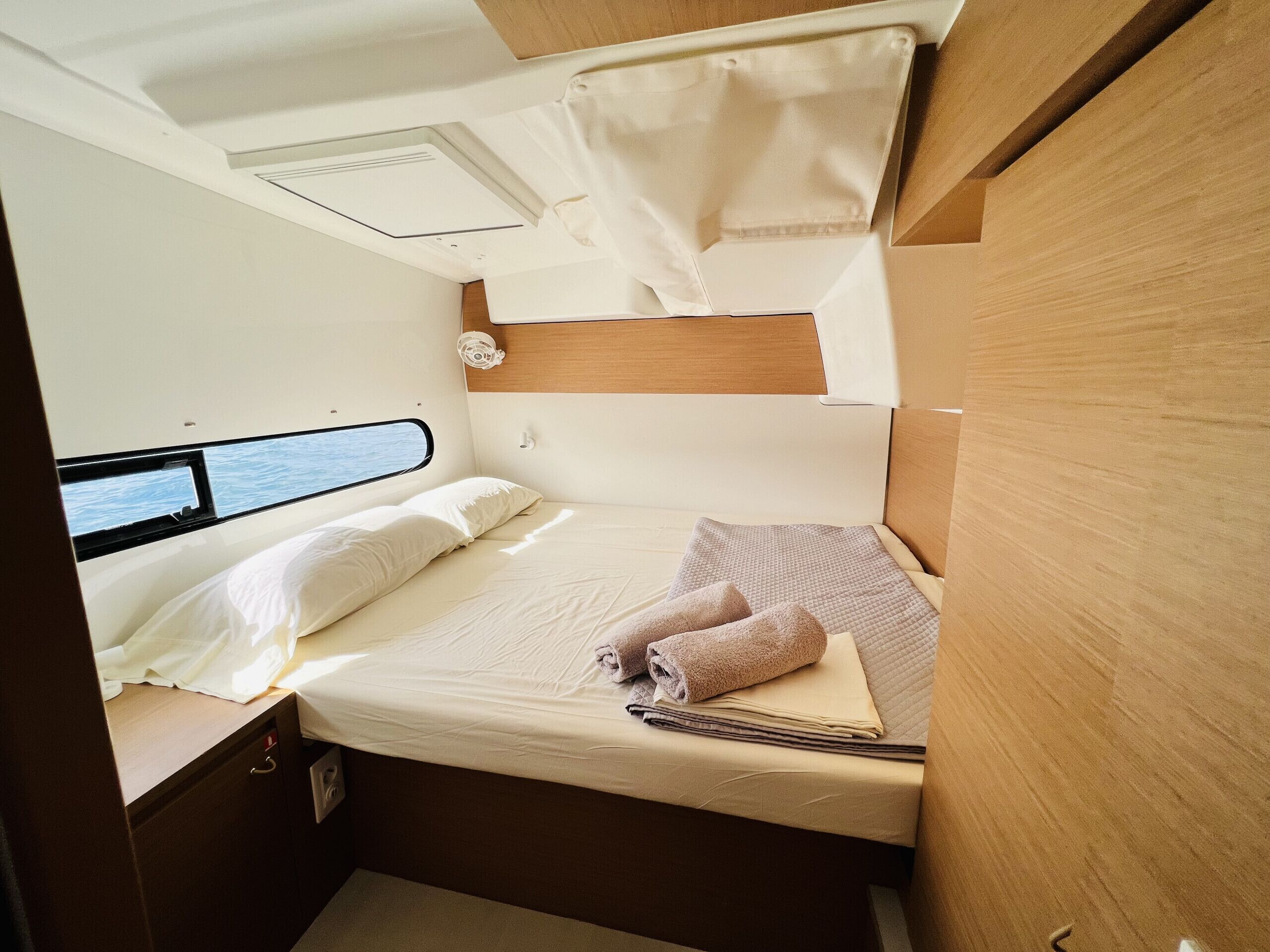 A compact, well-lit cabin with a bed, a small table, and a window offering a view of the water.