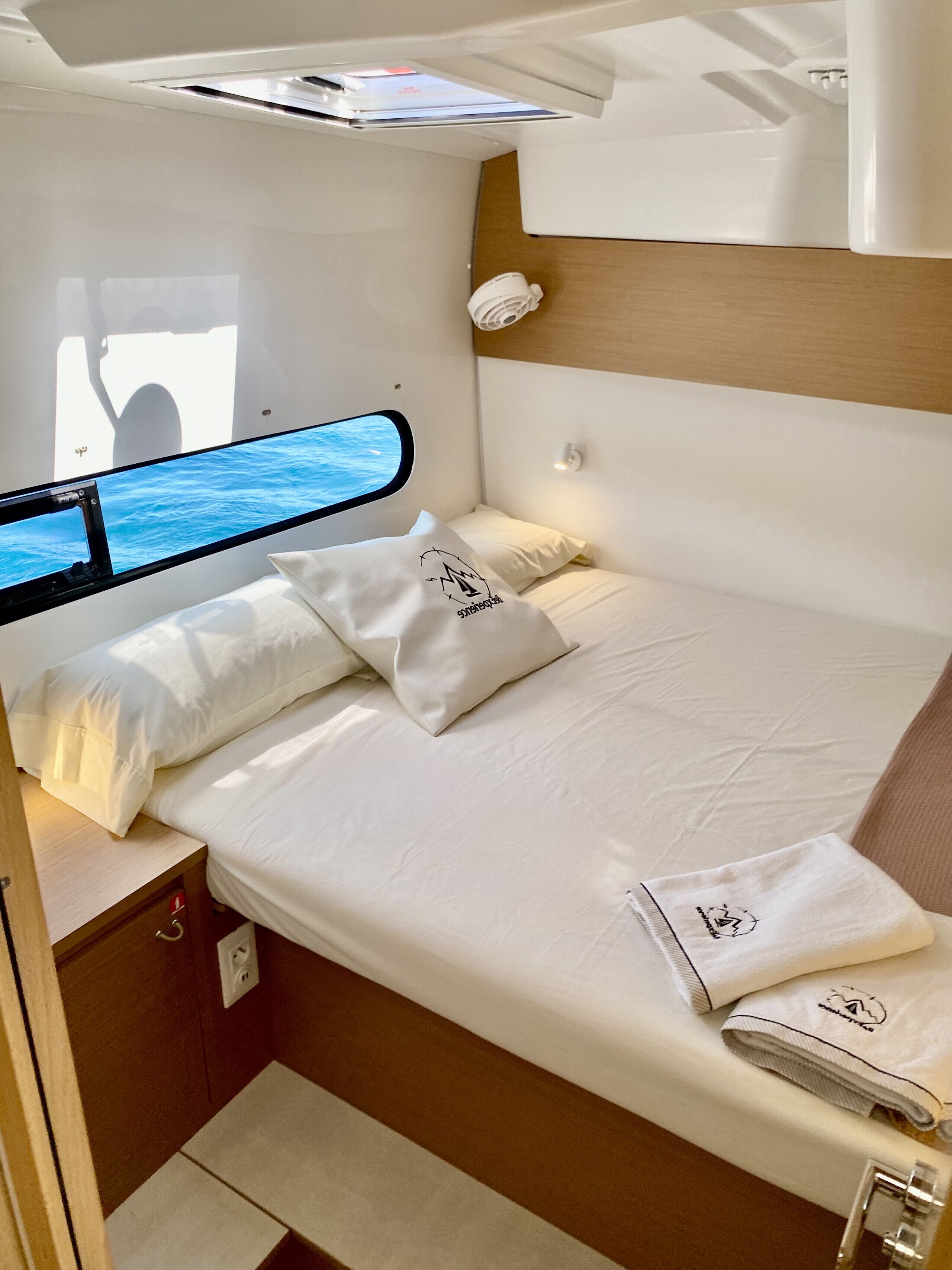 A compact, well-lit cabin with a bed, a small table, and a window offering a view of the sea.