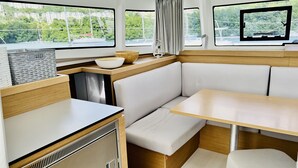 A compact interior with a kitchenette, seating area, and large windows offering views of greenery and buildings. - Sun-Kissed Sailing: A Luxurious Beach Experience in Valencia (Denia)