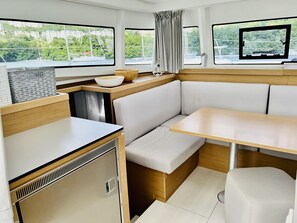 A compact interior with a kitchenette, seating area, and large windows offering views of greenery and buildings. - Sun-Kissed Sailing: A Luxurious Beach Experience in Valencia (Denia)