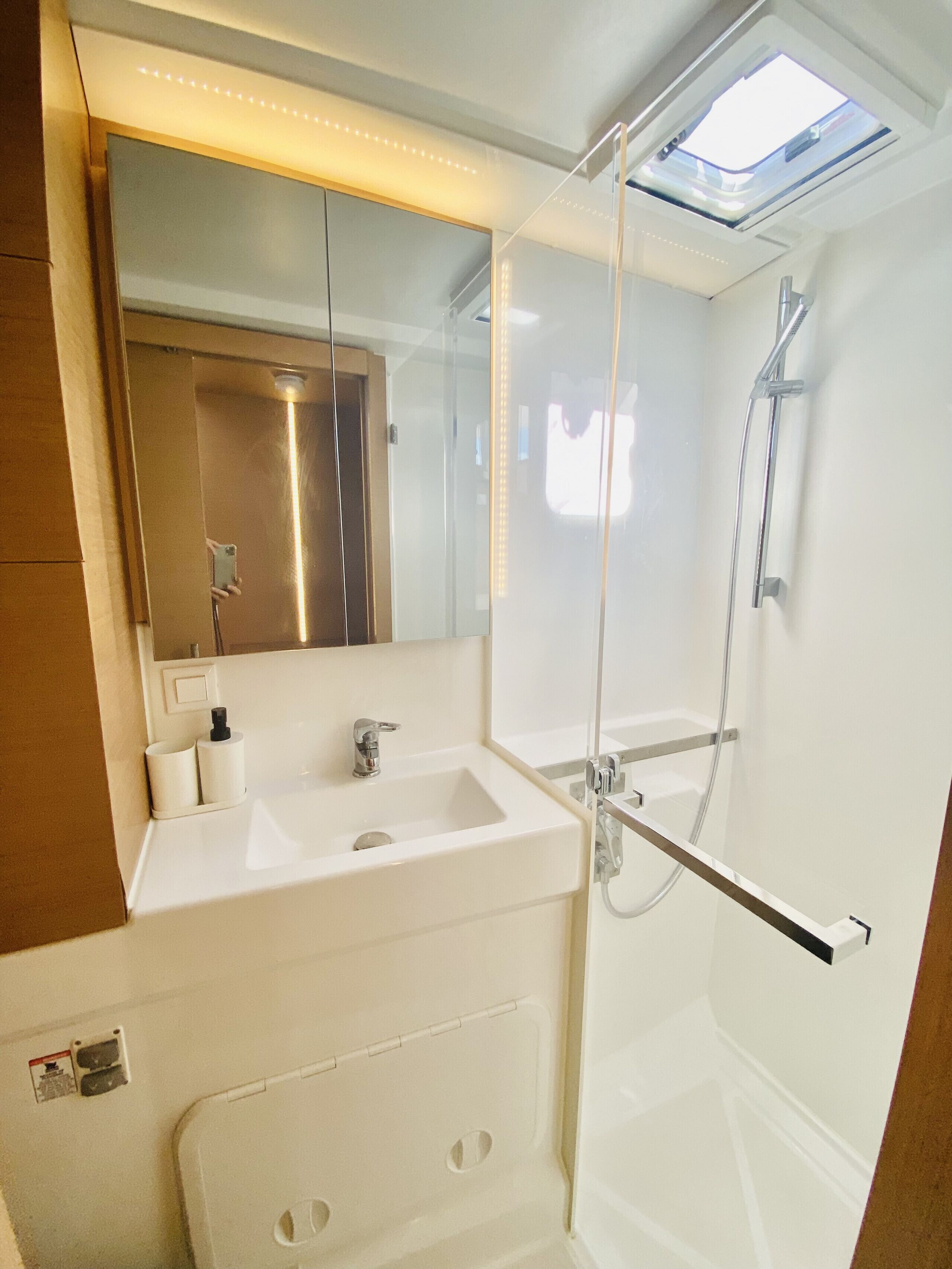 Une salle de bain moderne avec une douche à l’italienne en verre, un lavabo avec un miroir au-dessus et une fenêtre de toit.