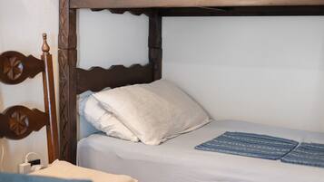 Un letto singolo con testiera in legno, un cuscino bianco e una coperta a motivi blu.