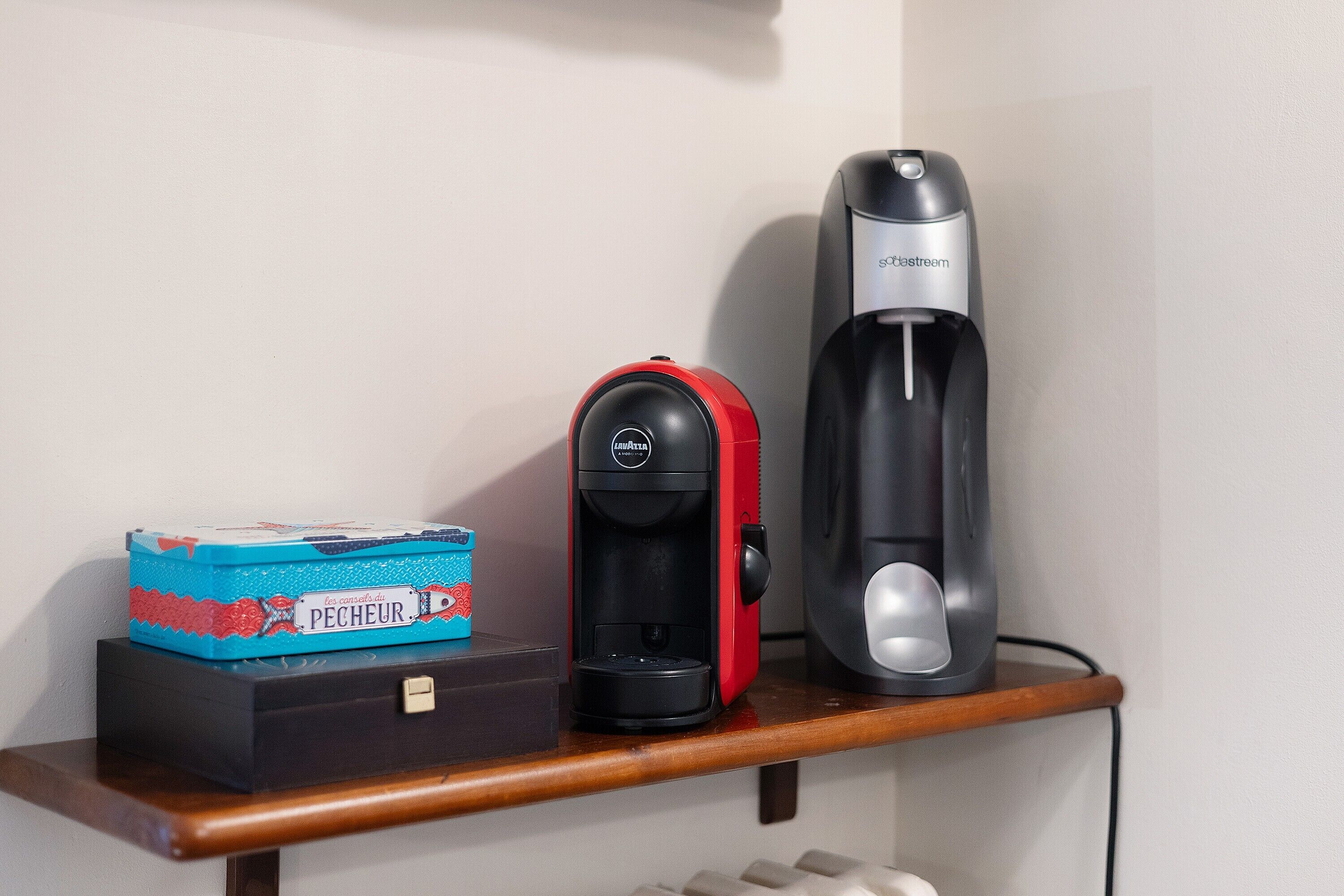 Une machine à café, une boîte étiquetée « Pêcheur » et un appareil noir posé sur une étagère en bois.