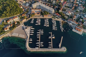 Vue aérienne d’une marina où sont amarrés des bateaux, entourée de bâtiments résidentiels et d’une zone boisée.