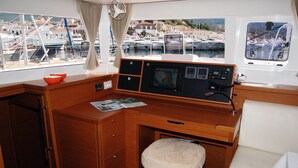 A cabin with a wooden desk, a cushioned stool, a control panel, and a view of a marina. - Sun-Kissed Sailing Adventure in Islas Sarónicas (Alimos)