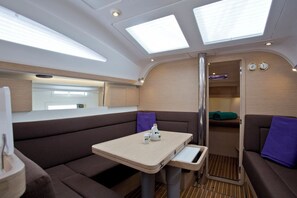 A compact interior with a dining area, cushioned seating, a small table, and a windowed passage. - Sun-Kissed Sailing Adventure in Istria, Croatia (Pula)