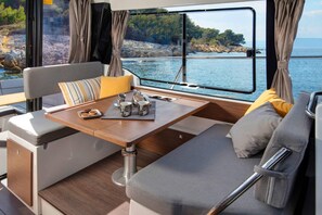 A boat interior with a dining area, cushioned seating, and a view of the water. - Sun-Kissed Sailing Adventure in Istria, Croatia (Pula)