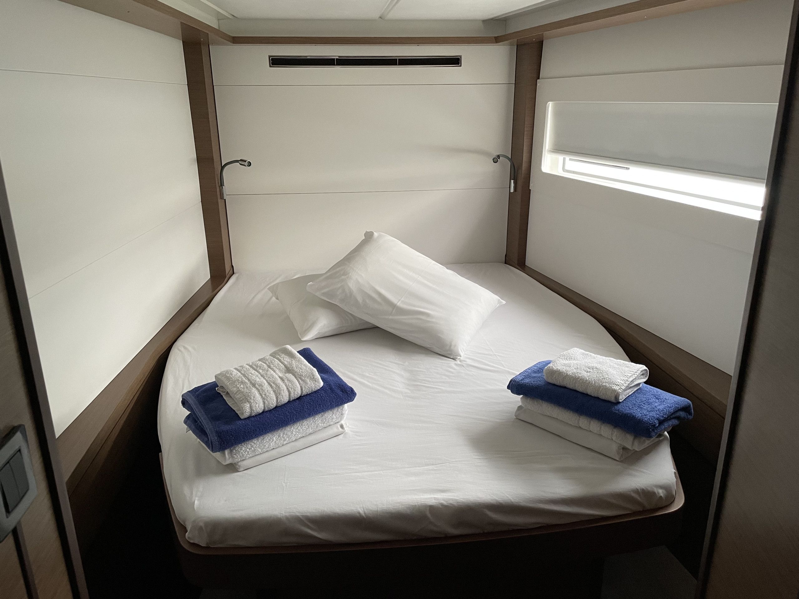 A small, single-bed room with a wooden headboard, white bedding, and two towels on the bed.