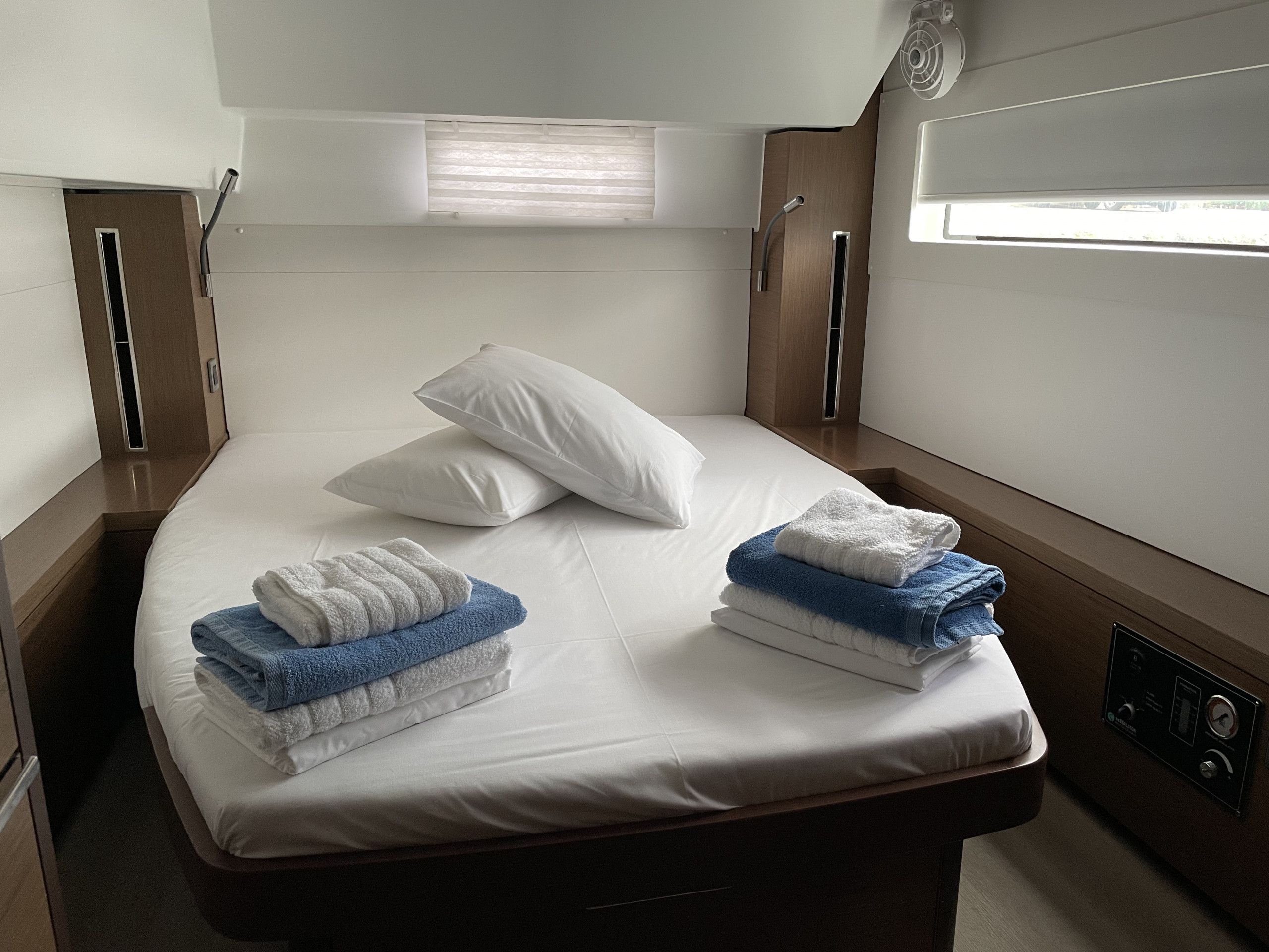 A single bed with white linens, two pillows, and folded towels in blue and white.