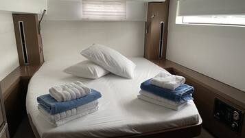 A single bed with white linens, two pillows, and folded towels in blue and white.