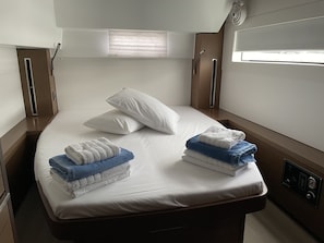 A single bed with white linens, two pillows, and folded towels in blue and white.
