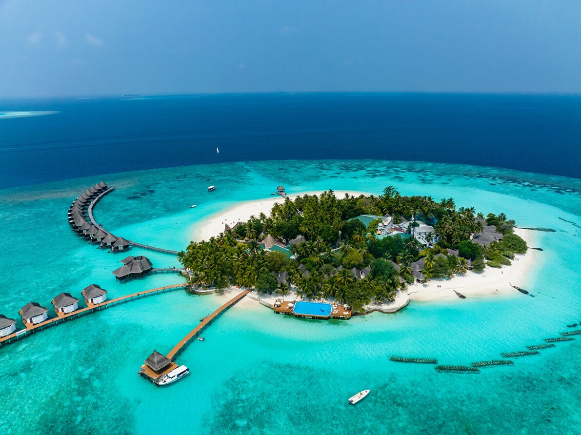 Vista aérea de un resort tropical con bungalows sobre el agua, un edificio central y aguas turquesas cristalinas.