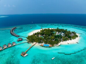 An aerial view of a tropical island resort with overwater bungalows, a central building, and clear turquoise waters.
