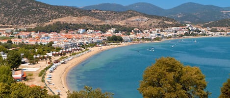 Un pueblo costero con playa, mar azul cristalino y montañas al fondo.
