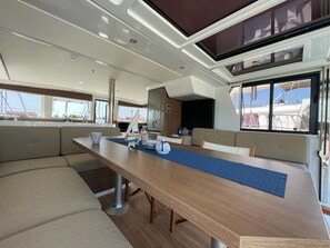 A modern interior with a long dining table, cushioned seating, and large windows offering views of the outside. - Sibenik Sun-soaked Sailing: A Luxurious Croatian Voyage (Pirovac)