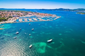 An aerial view of a coastal town with a marina, boats, and a clear blue sea.