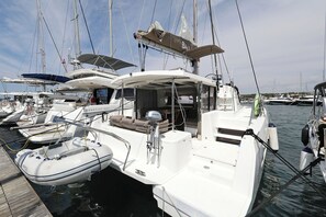 Eine Yacht liegt in einer Marina festgemacht, mit einem überdachten Deckbereich, einer Sitzecke und einem sichtbaren Steuerpult.