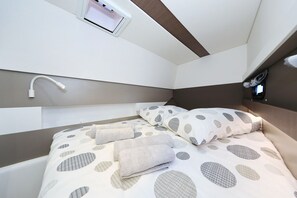 A compact bedroom with a bed, pillows, a wall-mounted light, and a small window.