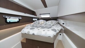 Ein kompakter, gut beleuchteter Innenraum mit einem Bett, Stauschubladen und einem kleinen Fenster.