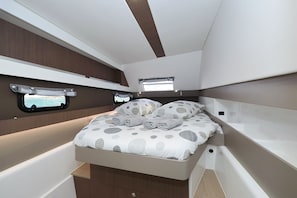 A compact, well-lit interior with a bed, storage drawers, and a small window.