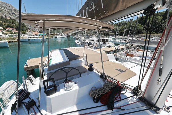 A sailboat docked at a marina with other boats, a clear sky, and a mountainous backdrop.