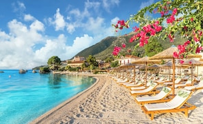 A beach with clear blue water, a sandy shore, and wooden lounge chairs under umbrellas. - Sun-Kissed Sailing Adventure in the Ionian Islands (Nikiana)