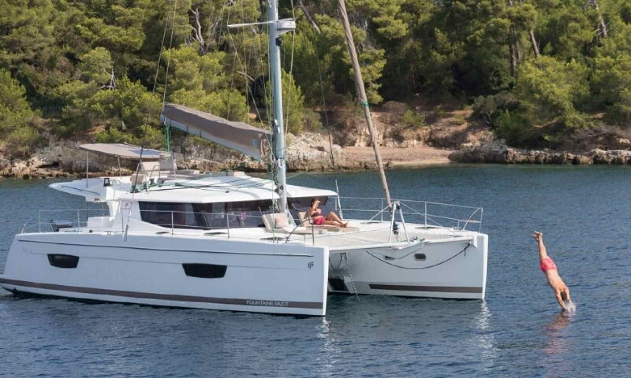 A white yacht with a covered deck, a person on the bow, and a woman diving into the water.