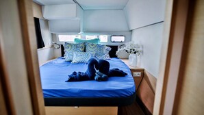A compact, well-lit room with a bed, pillows, a small bedside table, and a window.