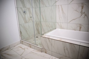 A bathroom with a glass-enclosed shower, a white bathtub, and marble tiles. - Softstay Ellipse Luxury Apartment (Johannesburg)