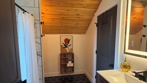 A bathroom with a wooden ceiling, a black hexagonal tile floor, a white sink with a mirror, and a shower curtain. - Cozy 2-bedroom house in adorable Mohnton with AC (Mohnton)