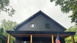 A dark wooden house with a porch, an American flag, and a number 7 sign. - Cozy 2-bedroom house in adorable Mohnton with AC (Mohnton)