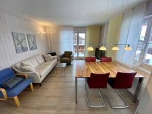 Ein modernes Wohnzimmer mit einem Holzesstisch, roten Stühlen, einem blauen Sofa und einem weißen Schlafsofa.