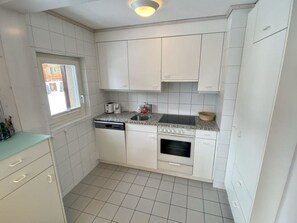 A compact kitchen with white cabinets, a built-in oven, a dishwasher, and a window providing natural light. - Suzanne Nr. 22 Appartement/Fewo, Dusche oder Bad, WC 4-Bettwohnung by Interhome (Gstaad)