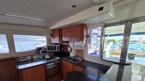 A compact kitchen with wooden cabinets, a microwave, a kettle, and a sink. - Caribbean Bliss: Sun-soaked Sailing Adventure from San Vicente y las Granadinas (Ribishi)