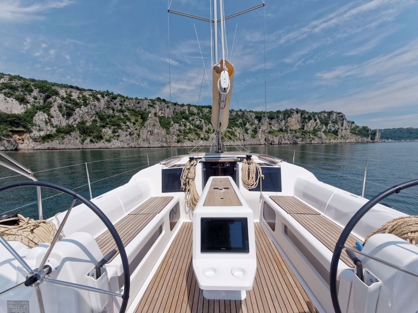 A boat's deck with a steering wheel, a control panel, and a view of a rocky coastline.