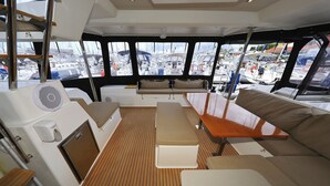 A boat interior with a wooden deck, cushioned seating, and a view of other boats through large windows. - Sun-Kissed Sailing Adventure in Zadar, Croatia (Biograd na moru)