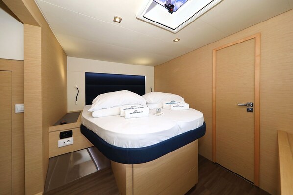 A compact room with a bed, a small bedside table, a built-in TV, and a door.