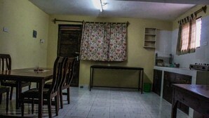 Un comedor con una mesa y sillas, un banco, una ventana con cortinas florales y una zona de cocina con armarios y un fregadero.