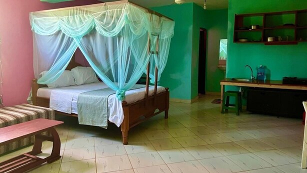 Una habitación con una cama con dosel, un banco, una mesita y una pequeña cocina.