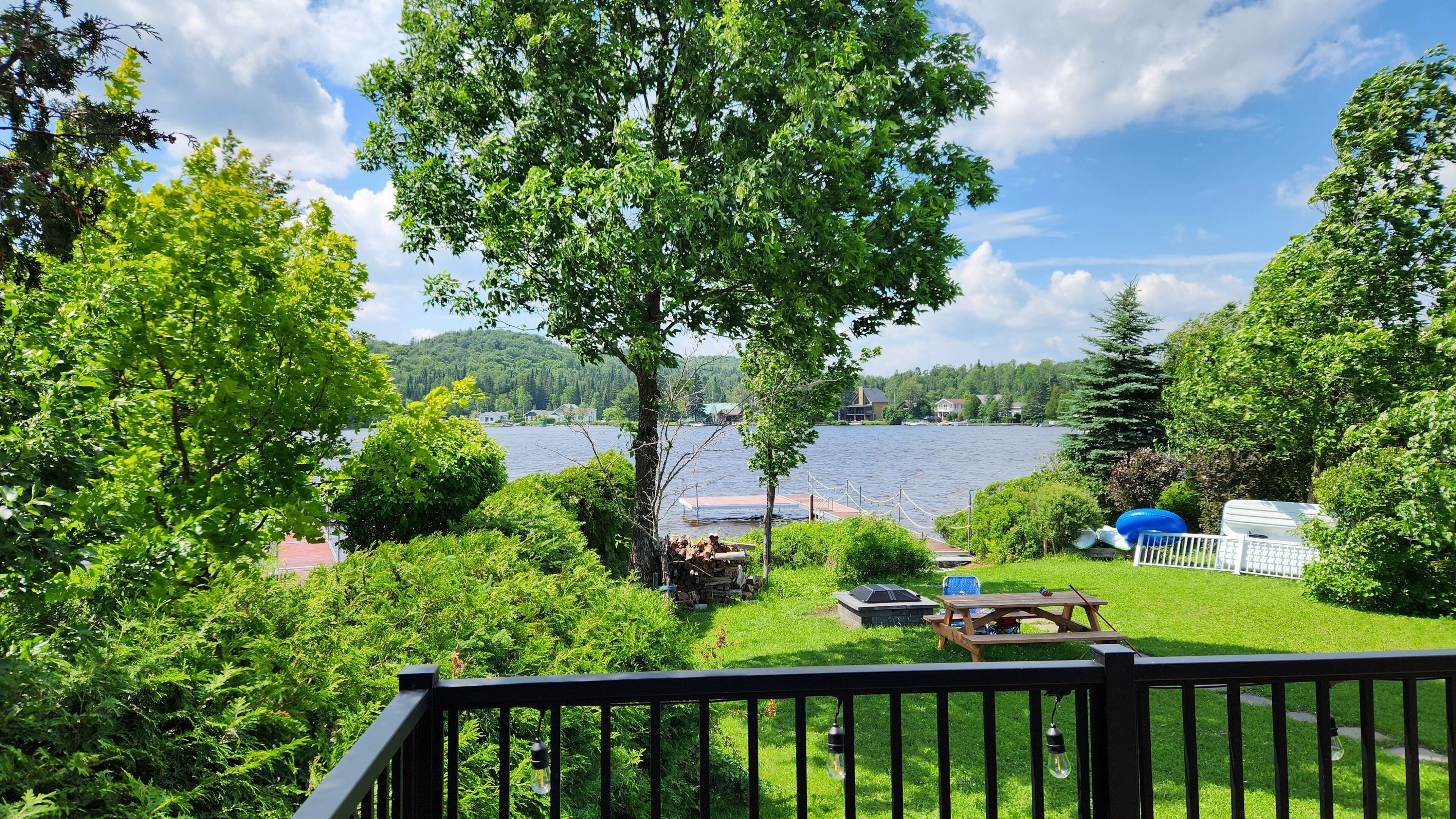 Une vue sur le lac, avec un quai, un espace pique-nique et une végétation luxuriante tout autour.