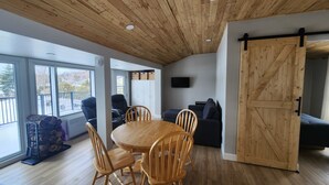 Ein modernes Interieur mit Holzboden, einem Essbereich mit Holzstühlen, einer Couch und einer Schiebetür im Bauernhausstil.