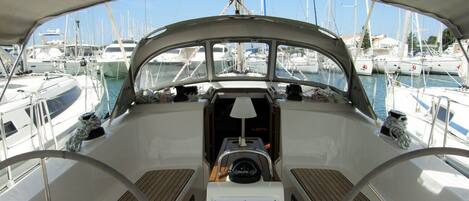 Le pont d’un bateau, avec un volant, une console centrale et une vue sur les autres bateaux amarrés dans la marina.
