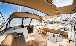 A yacht's deck with a steering wheel, navigation equipment, and a dining area with a table, chairs, and a book.