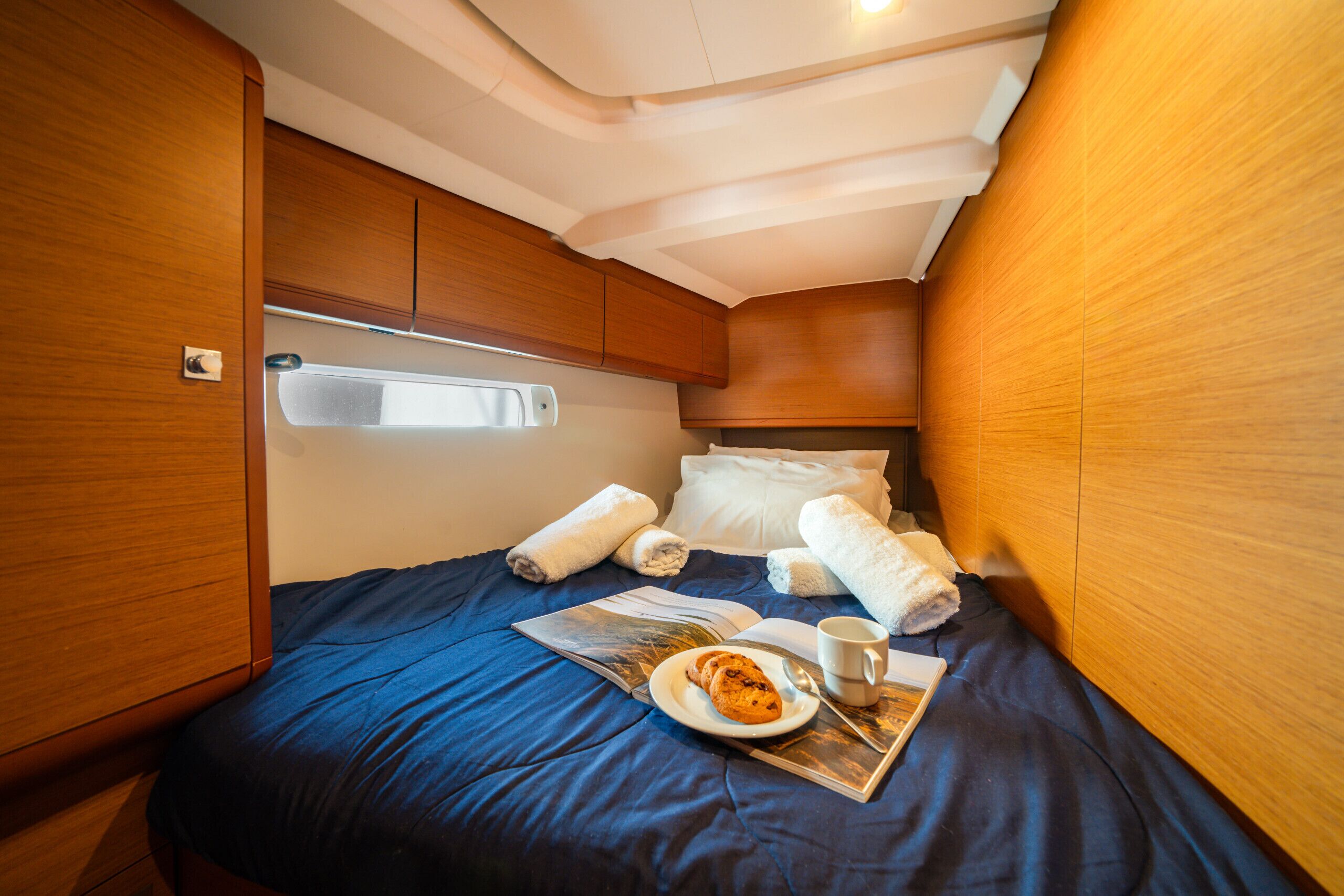 Une chambre à coucher de taille réduite, comprenant un lit, des oreillers, des serviettes, une assiette avec de la nourriture, une tasse et un magazine.