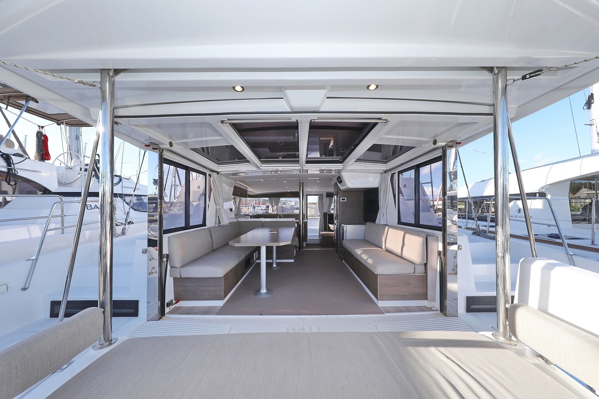 A boat's interior with a dining area, seating, and a view of other boats.