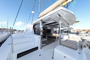 A white yacht with a covered deck area, a seating arrangement, and a view of other yachts in the marina. - Sibenik Sun and Beach Sailing Extravaganza: A Croatian Coastal Adventure (Vodice)