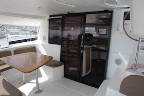A boat interior with a table, chairs, a sliding door, and a control panel.
