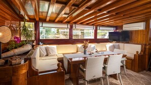 A cozy cabin interior with a wooden ceiling, a sofa, a dining table, and a TV. - Sun-Kissed Sailing Adventure in Split, Croatia (Kaštel Gomilica)